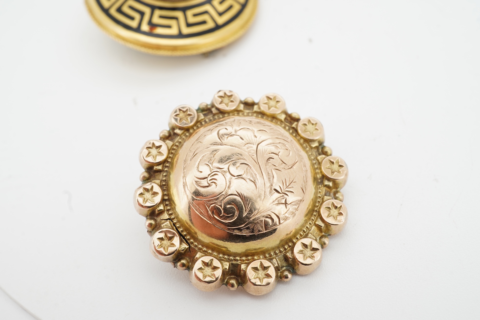 Three brooches, comprising: a Victorian circular brooch centring on a cabochon onyx set with a rose-cut diamond in a star setting, to concentring bands of seed pearls and Greek key motifs in black enamel, the reverse wit